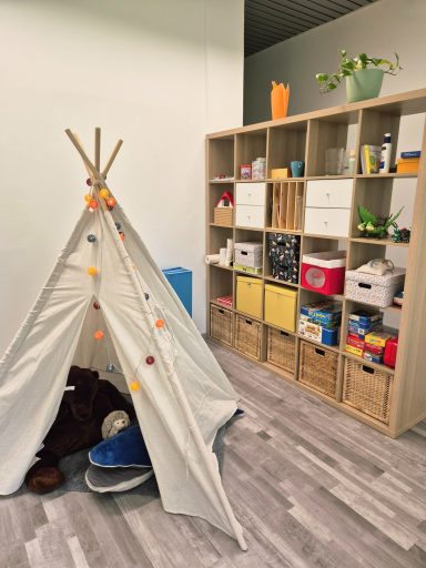 Ein Spielzelt aus Stoff steht neben einem Regal mit viel Therapiematerial und Spielzeug