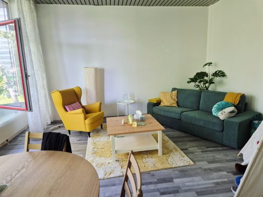 Gemütliches Wohnzimmer mit grüner Couch, gelber Armlehne und hellem Holztisch.