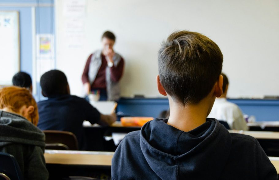 Schüler schaut auf einen Lehrer, der im Klassenzimmer an der Tafel steht.