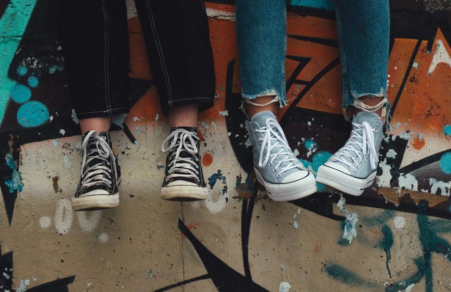 Zwei Paare Sneakers auf graffiti-bedecktem Boden, eines schwarz, das andere hellgrau.