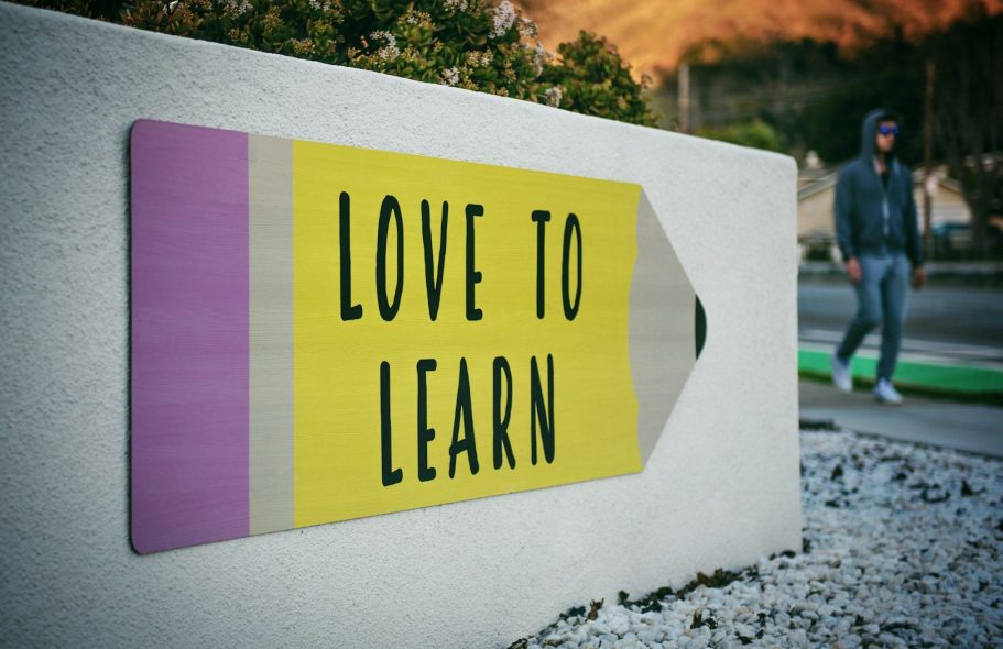 Ein gelbes Schild mit der Aufschrift "LOVE TO LEARN" und einer Person im Hintergrund.